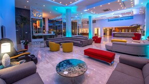 A spacious lobby with a modern design, featuring a large sectional sofa, a red ottoman, and a unique glass coffee table. - Nicholas Color Hotel (Ayia Napa)