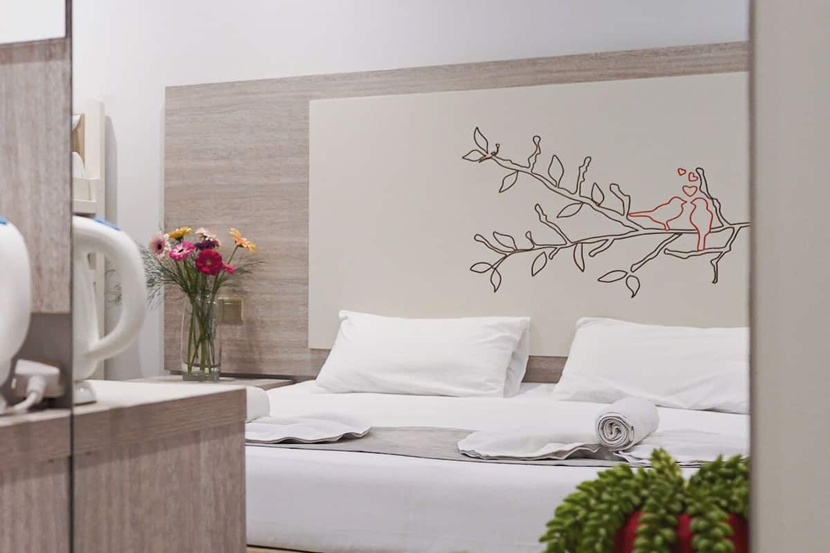 A modern hotel room with a bed, a desk, a mirror, and a decorative wall art.