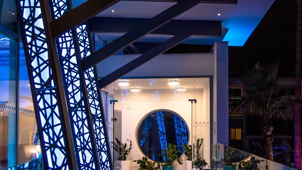 A modern building entrance with a wooden floor, a glass railing, and a decorative metal structure. - Nicholas Color Hotel (Ayia Napa)