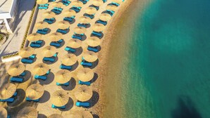 Luftaufnahme eines Strandes mit Reihen von Liegestühlen und Reetdachschirmen.