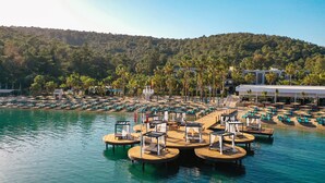 Ein Resort mit Poolbereich, der Holzplattformen zum Liegen mit Liegestühlen und Sonnenschirmen umfasst, umgeben von Palmen und einer Bergkulisse.