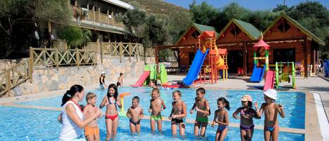 A swimming pool area with a wooden building, slides, and a fenced deck.