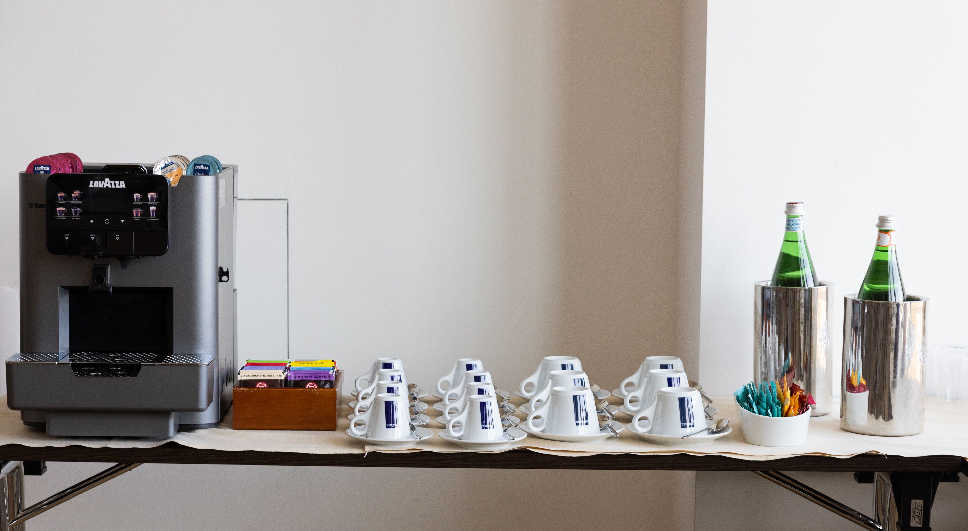 A coffee machine, a stack of books, and a row of white cups and saucers on a table.