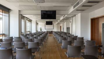 Una sala conferenze con file di sedie, un proiettore e un grande schermo.