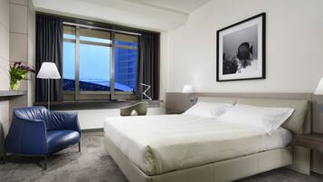 Una habitación de hotel con una cama grande, una silla azul, un escritorio y una ventana con vista a la ciudad.
