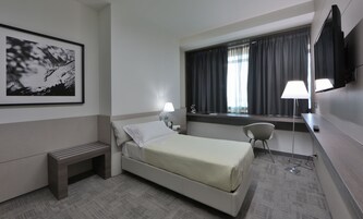 Una camera d'albergo con un letto, comodino, lampada, sedia e televisore appeso al muro.