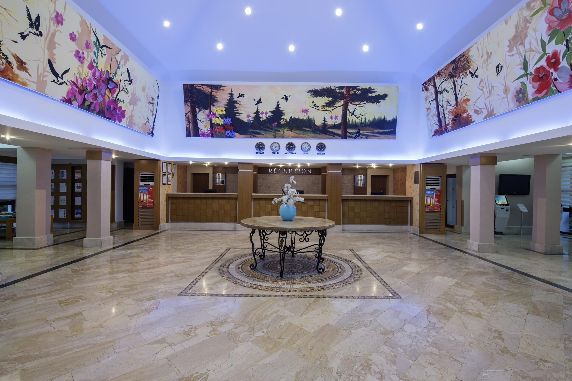 Een hotel lobby met een receptiebalie, een ronde centrale tafel en een groot muurdecoratie aan het plafond.