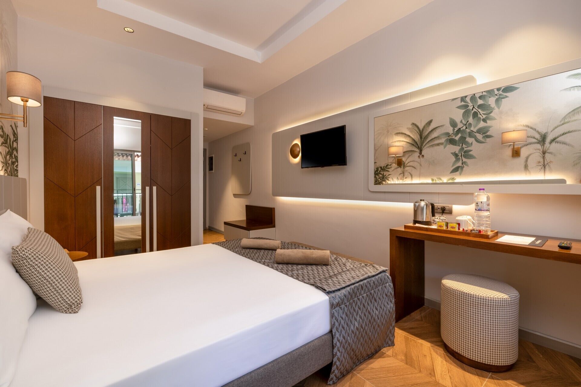 A hotel room with a bed, a desk, a TV, and a large mirror.