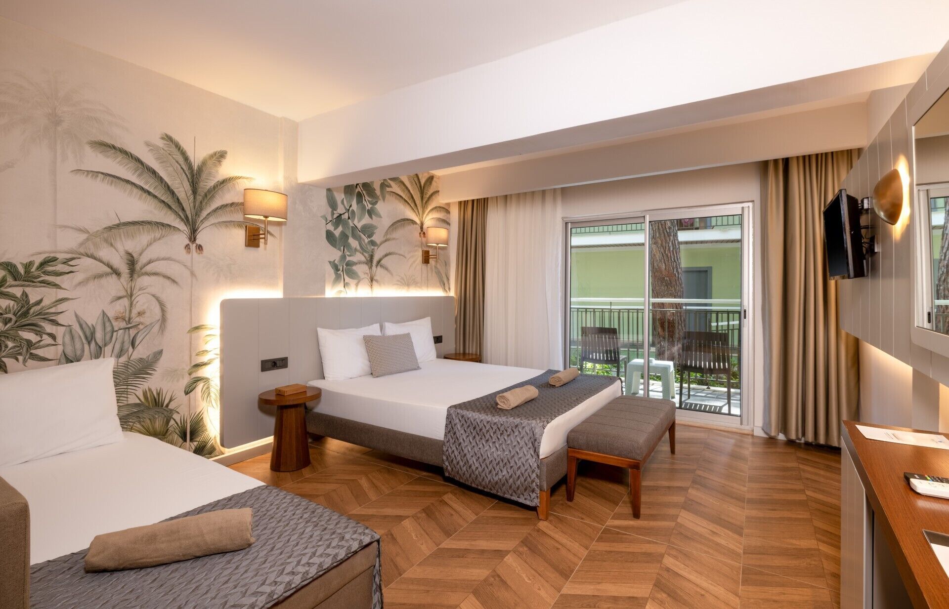 A hotel room with a bed, a sofa, a desk, a TV, and a balcony with a view.
