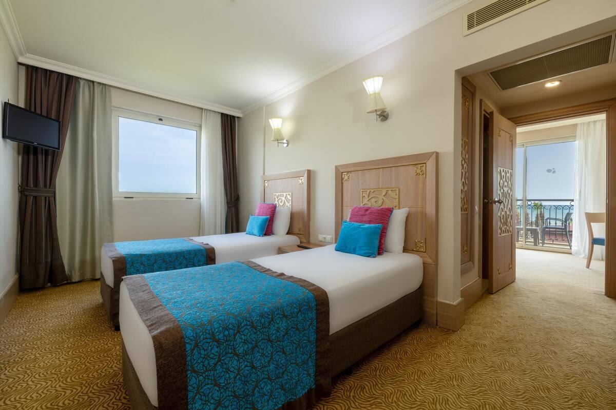 A hotel room with two beds, a television, a balcony, and a door leading to another room.
