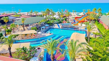 Relax by the pool surrounded by lush greenery and palm trees, with a scenic ocean view nearby.