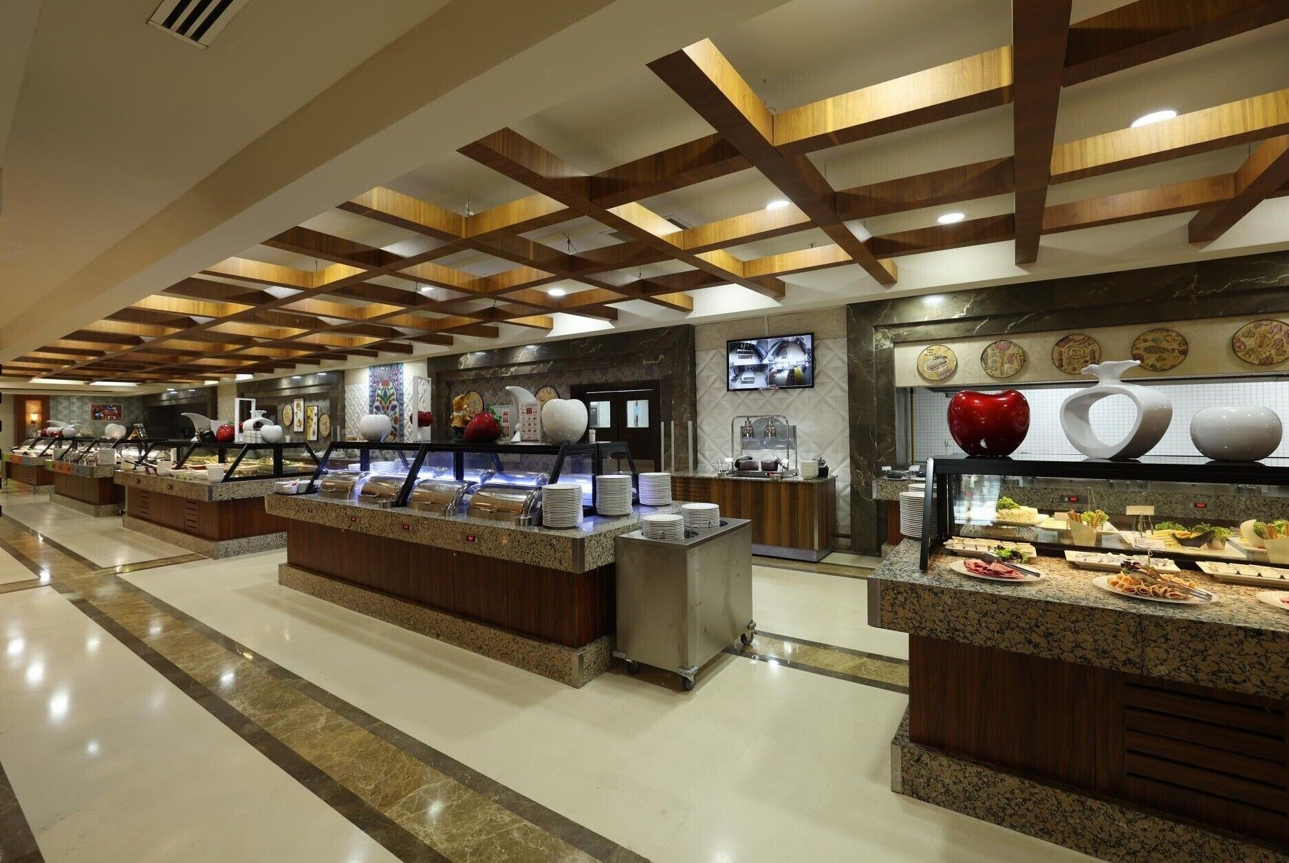 A hotel buffet with multiple serving stations, a television mounted on the wall, and a decorative wall with plates.