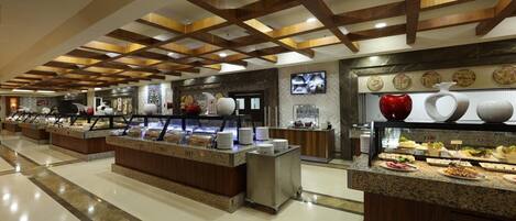 A hotel buffet with multiple serving stations, a television mounted on the wall, and a decorative wall with plates.