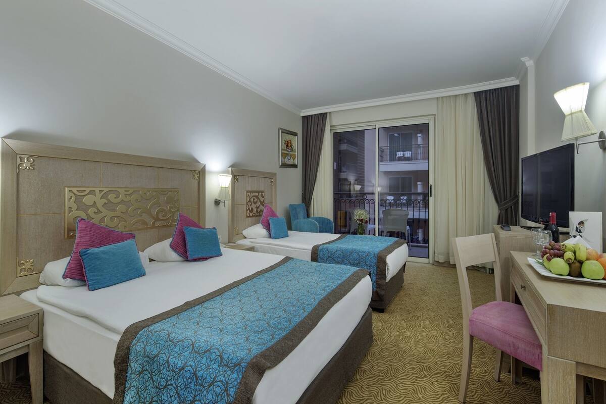 A hotel room with two beds, a desk, a chair, a mirror, and a balcony view.