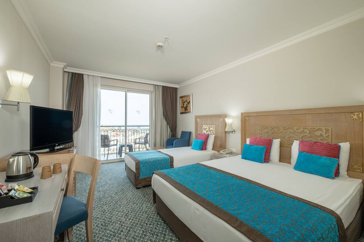 A hotel room with two beds, a TV, a desk with a coffee maker, and a balcony with a view.