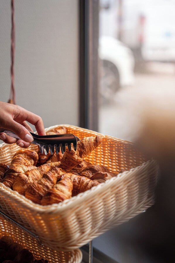 A hand using a spatula to serve croissants from a wicker basket.