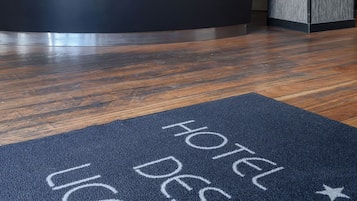 Ein Hotelrezeptionstresen mit dunklem Holzboden und einer blauen Matte mit der Aufschrift 'HOTEL DES LIS'.