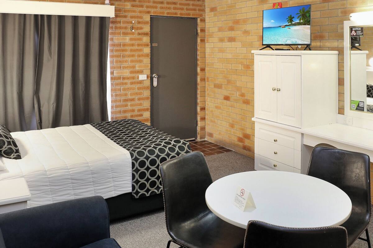 A hotel room with a bed, a desk, a chair, a round table, a mirror, and a TV on a cabinet.