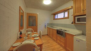 A compact kitchen with wooden cabinets, a microwave, a stove, and a refrigerator. - Cousins Motor Inn (Inverell)