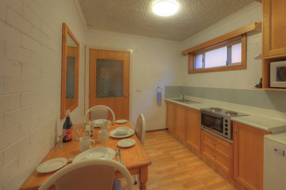 A compact kitchen with wooden cabinets, a microwave, a stove, and a refrigerator.