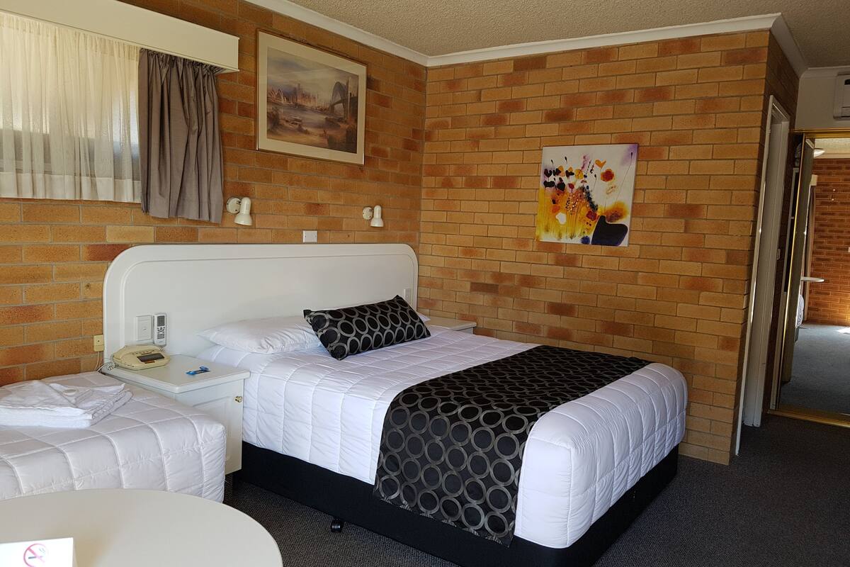 A hotel room with a brick wall, a bed with white bedding, a bedside table with a phone, and a painting above the bed.