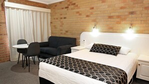 A hotel room with a brick wall, a bed with a patterned bedspread, a desk with a chair, and a window with curtains. - Cousins Motor Inn (Inverell)