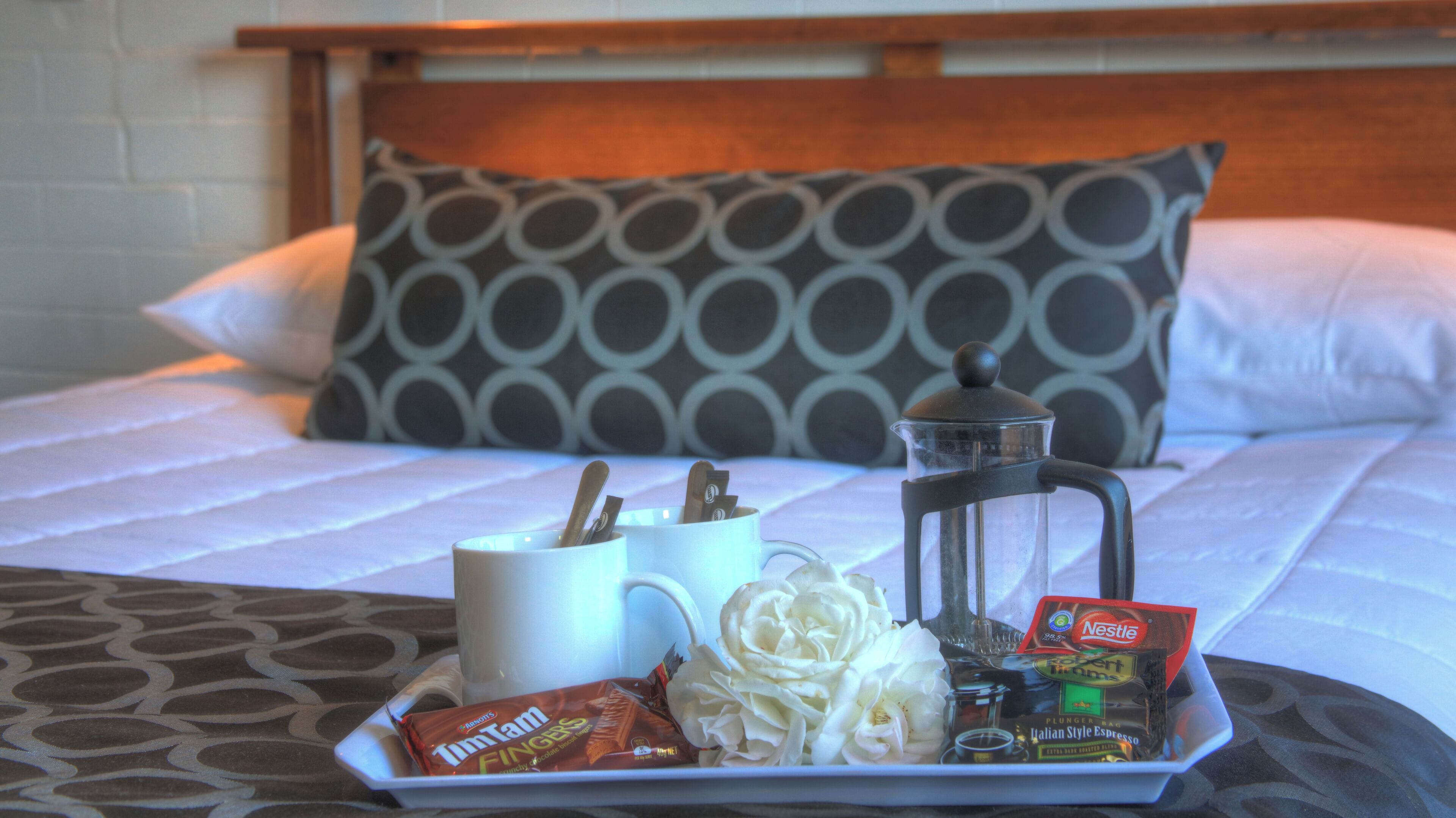 Een ontbijfwagen op een bed met een koffiezetapparaat, een mok, Tim Tams en een pakje oploskoffie.