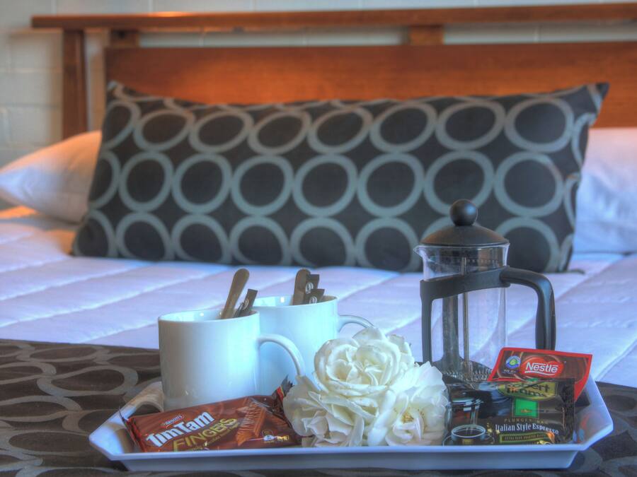 A breakfast tray on a bed with a coffee maker, a mug, Tim Tams, and a packet of instant coffee.