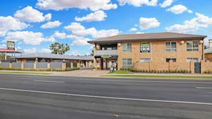 A Cousins Motor Inn with a reception area, a parking lot, and a clear blue sky with clouds. - Cousins Motor Inn (Inverell)