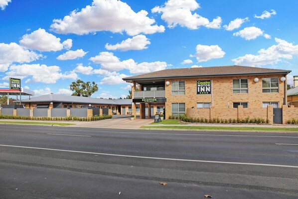 A Cousins Motor Inn with a reception area, a parking lot, and a clear blue sky with clouds.