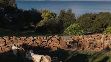 A wicker chair with a cushion and a bowl on a stone wall overlooking a body of water with mountains in the distance.
