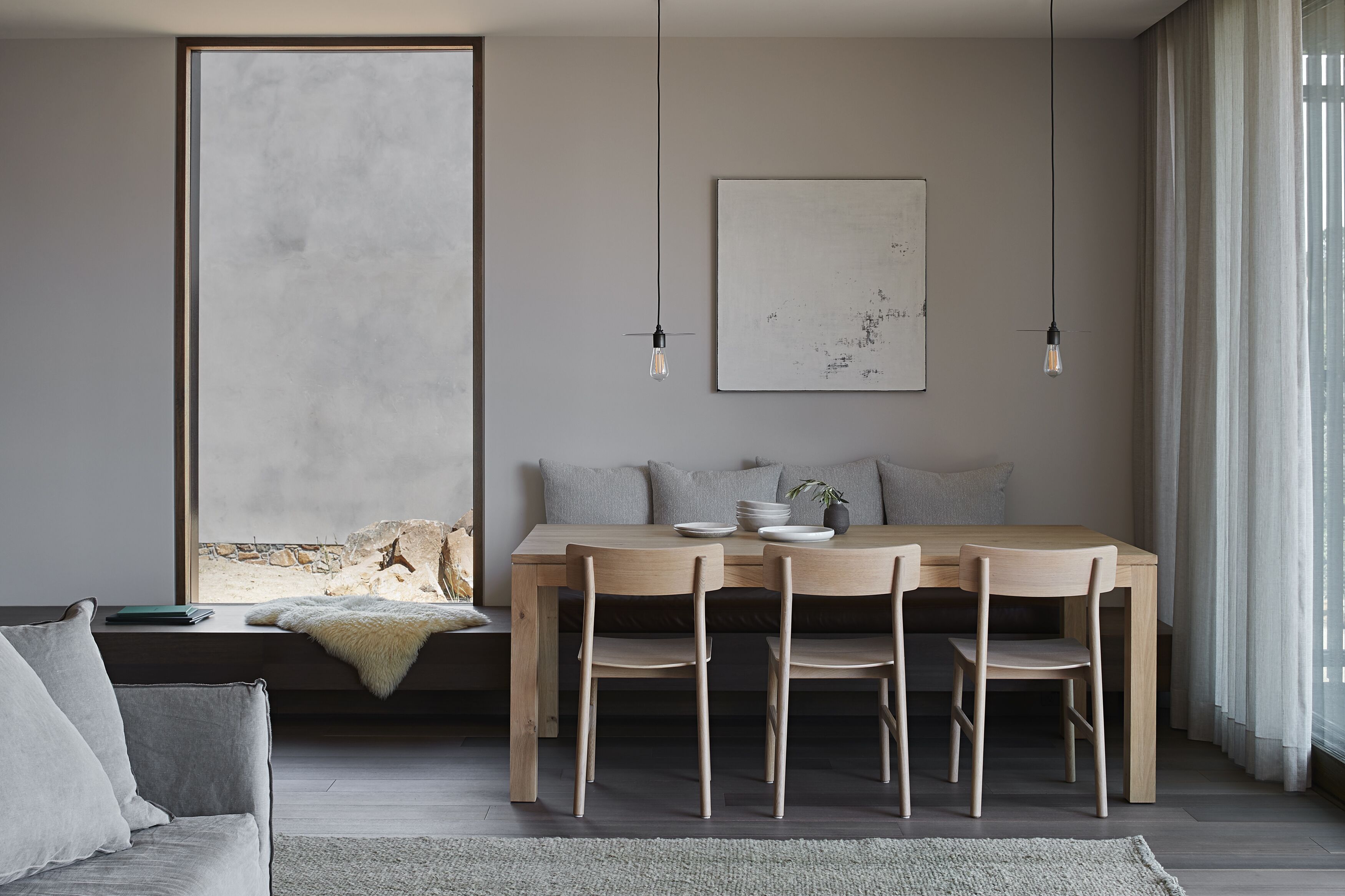 Uma área de jantar moderna com uma mesa de madeira, quatro cadeiras e uma janela grande com cortinas.