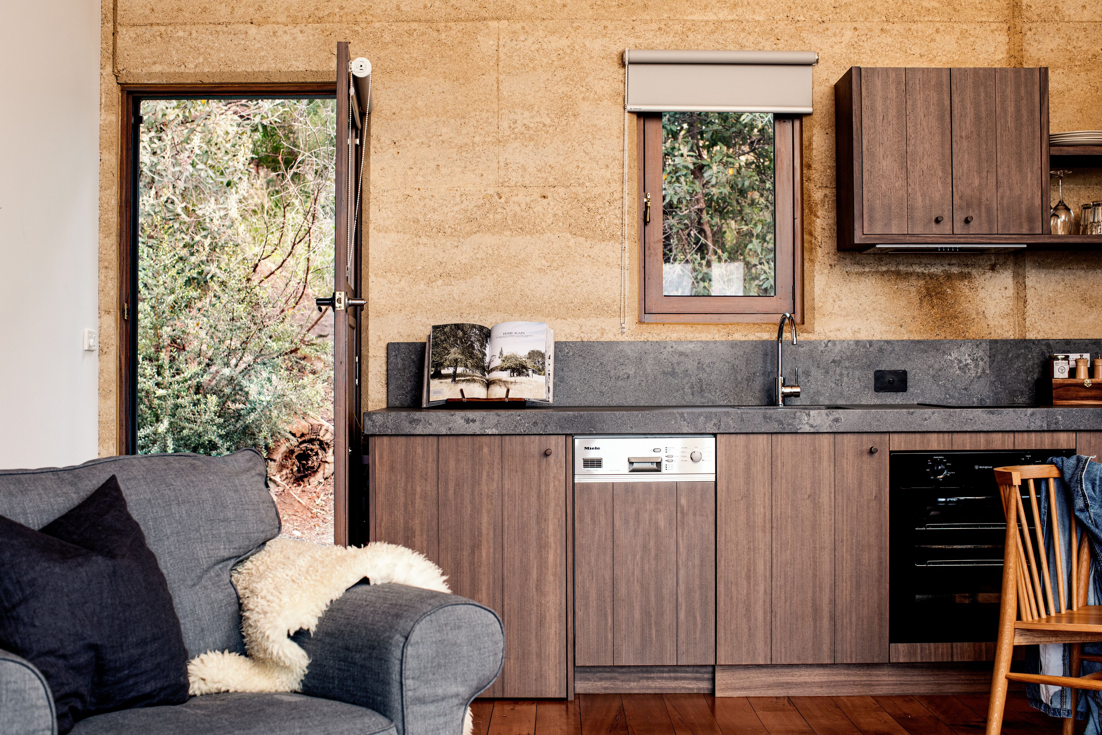 A modern kitchen with wooden cabinets, a built-in dishwasher, and a window overlooking greenery.