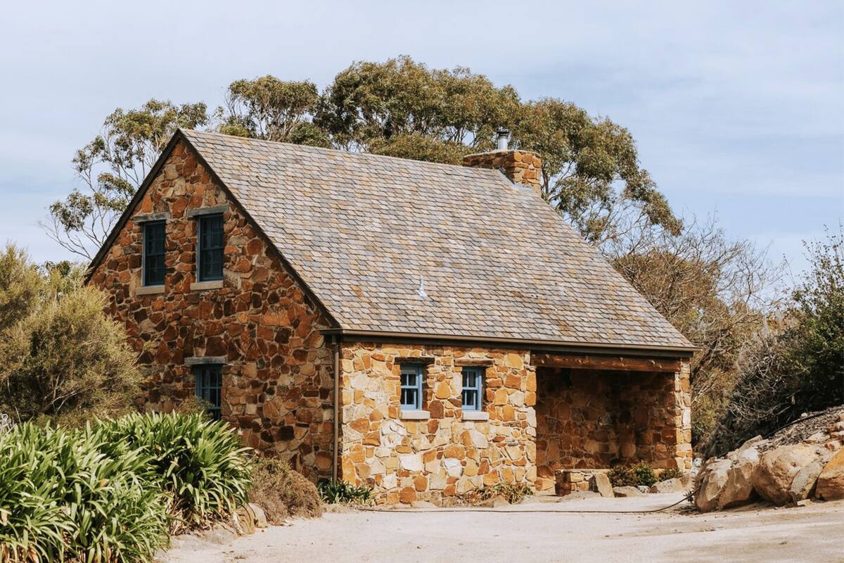 A stone house with a sloped roof, two windows, and a chimney.