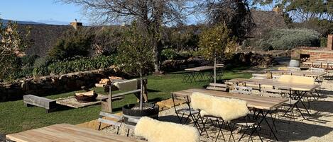 An outdoor seating area with wooden tables and chairs, surrounded by gravel and greenery.