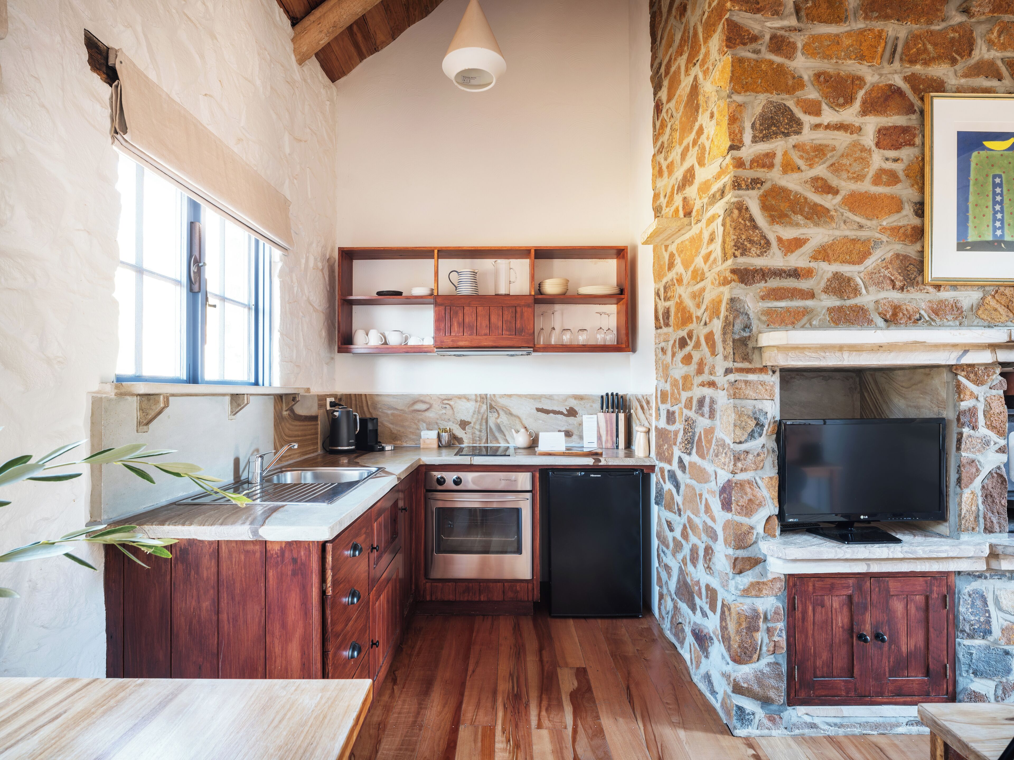 Una cocina compacta con armarios de madera, una pared de piedra y una televisión empotrada.