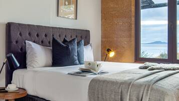 A bedroom with a large bed, a wooden ceiling, a view of the sea, and a framed picture on the wall.