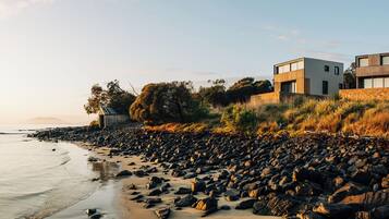 A modern coastal property with a large beach view, featuring a two-story building with a stone foundation and wooden accents.