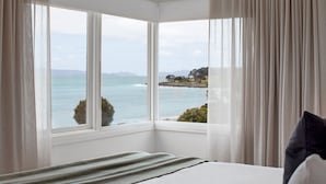 Een slaapkamer met een groot erkerraam met uitzicht op de kust.
