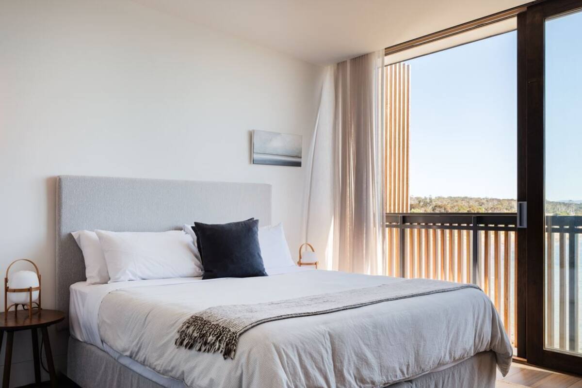 A bedroom with a large bed, a nightstand, a chair, and a view of the outdoors through a sliding door.