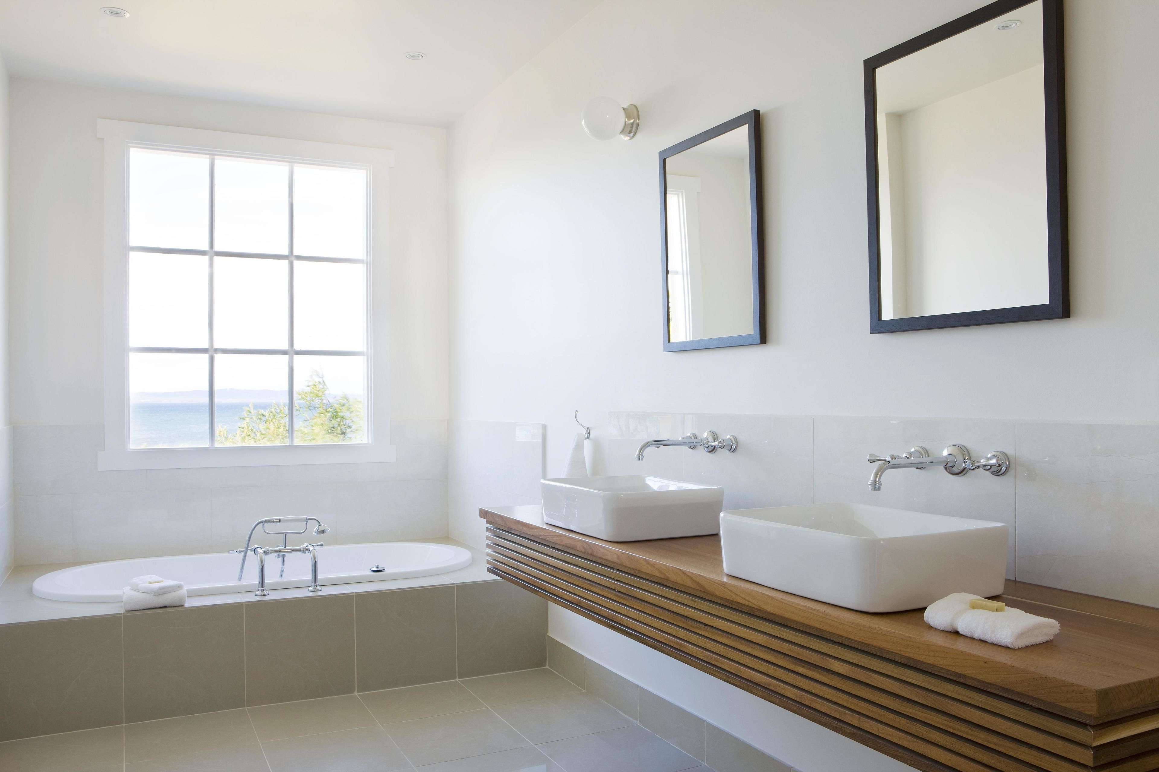 A modern bathroom with a bathtub, two sinks, and a window with a view.