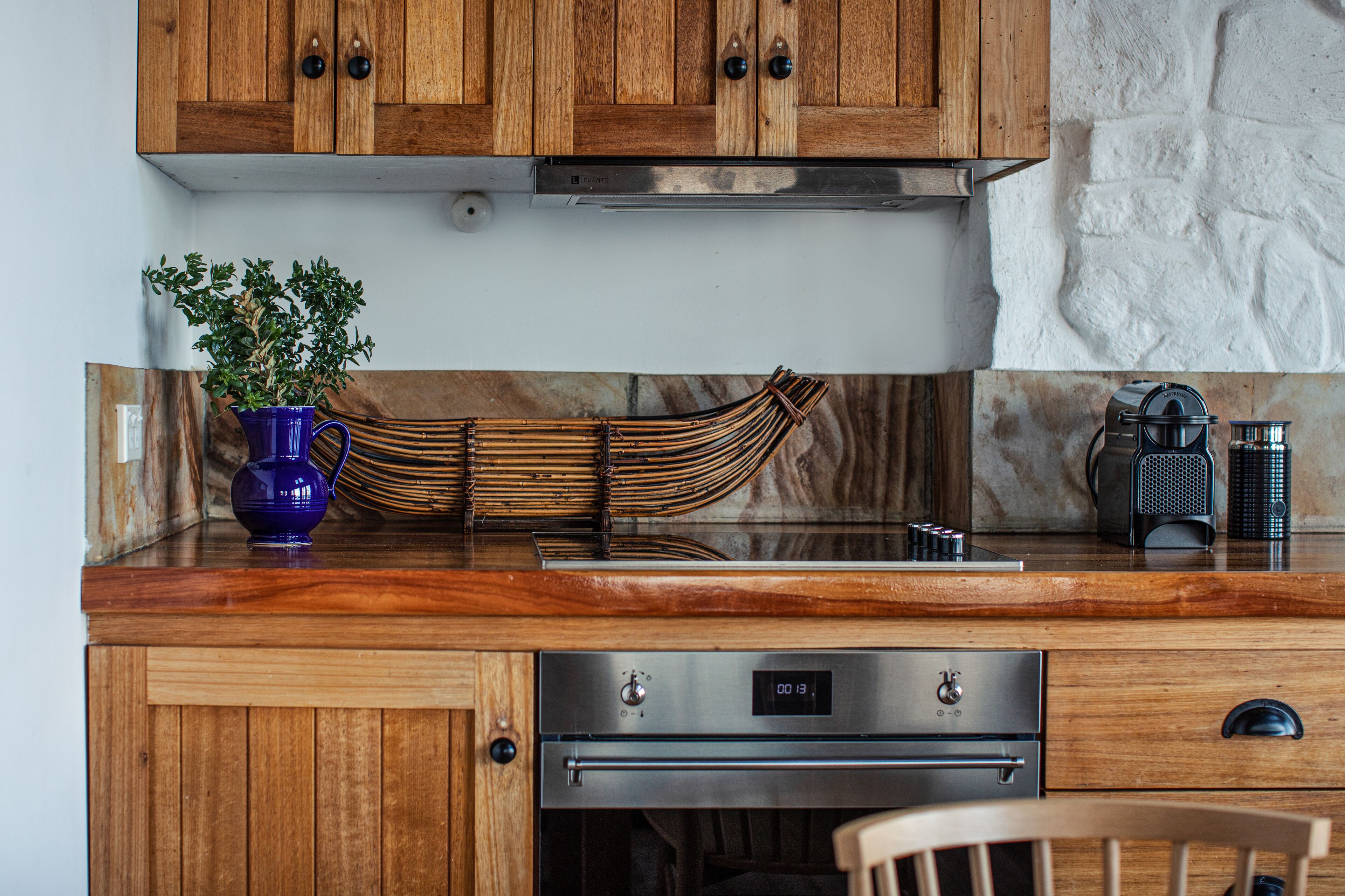 Une cuisine avec des meubles de rangement en bois, un four en acier inoxydable et un vase bleu contenant une plante.
