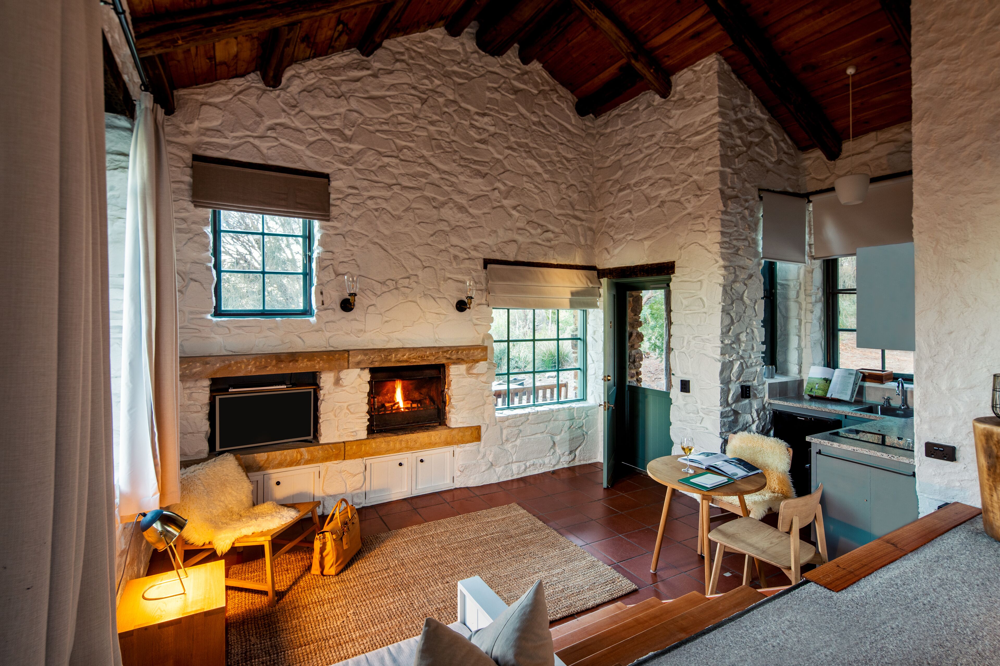 A rustic interior with a stone wall fireplace, wooden furniture, and a kitchen area.