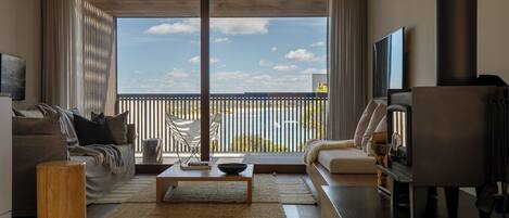 Una sala moderna con sofá, mesa de centro y televisor. Amplias ventanas ofrecen vistas al exterior.