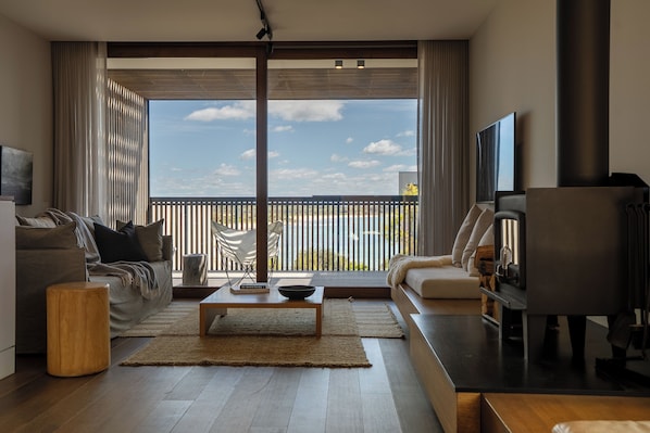 A modern living room with a sofa, coffee table, and TV. Large windows offer a view of the outdoors. - Piermont Retreat Swansea (Swansea)