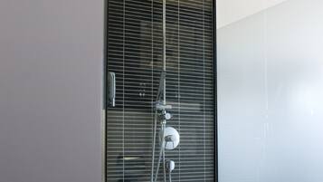 Un baño moderno con mampara de vidrio, ducha con cabezal de ducha manual y un inodoro.