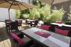An outdoor patio with wicker furniture, glass tables, and a large umbrella.