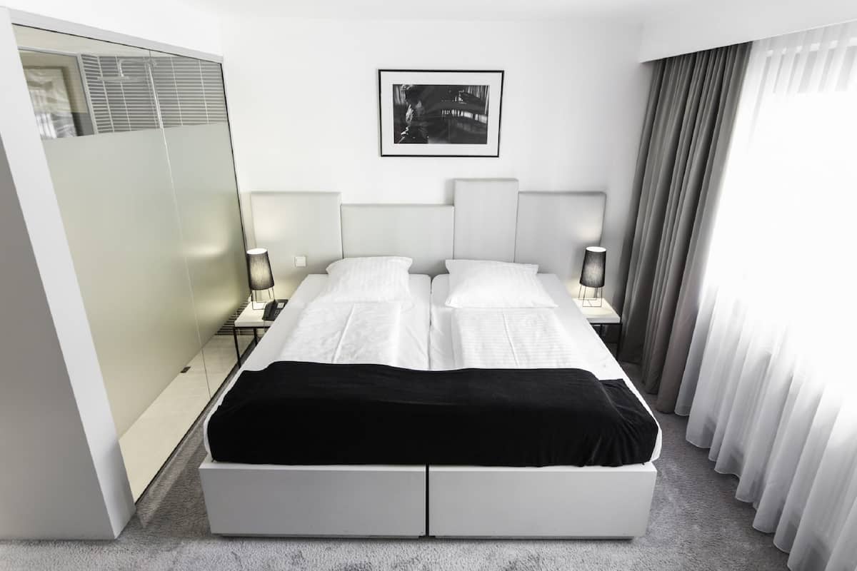 A modern bedroom with a large bed, bedside tables, a framed picture on the wall, and a sliding glass door.