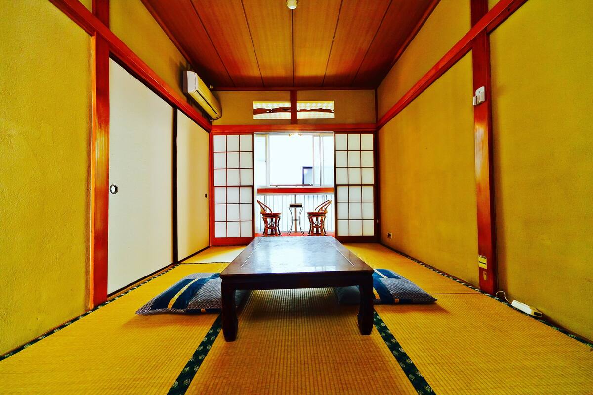 Una habitación japonesa tradicional con suelo de tatami, una mesa baja y puertas correderas.