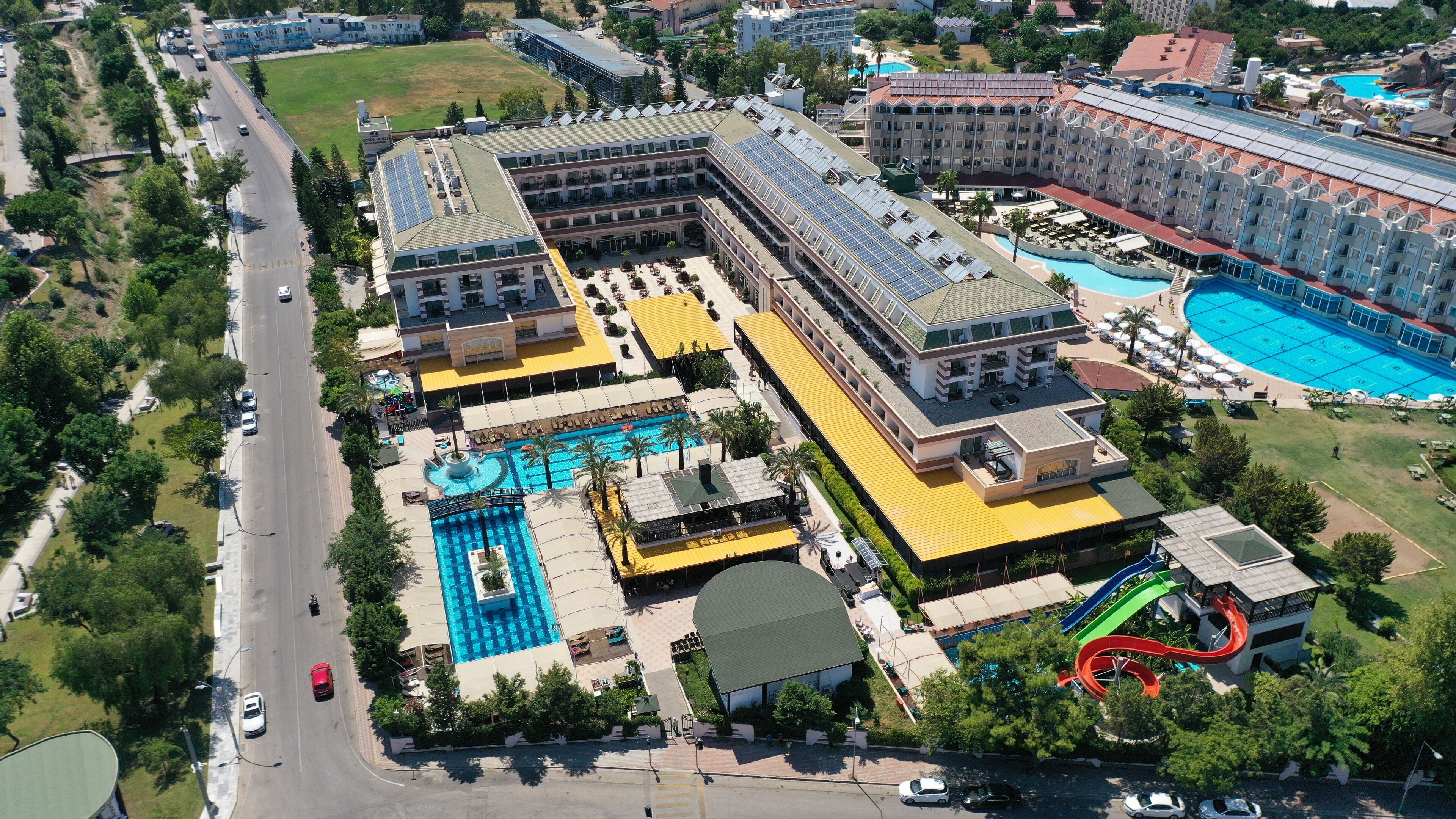 A large hotel with multiple swimming pools, a water slide, and a road with cars.